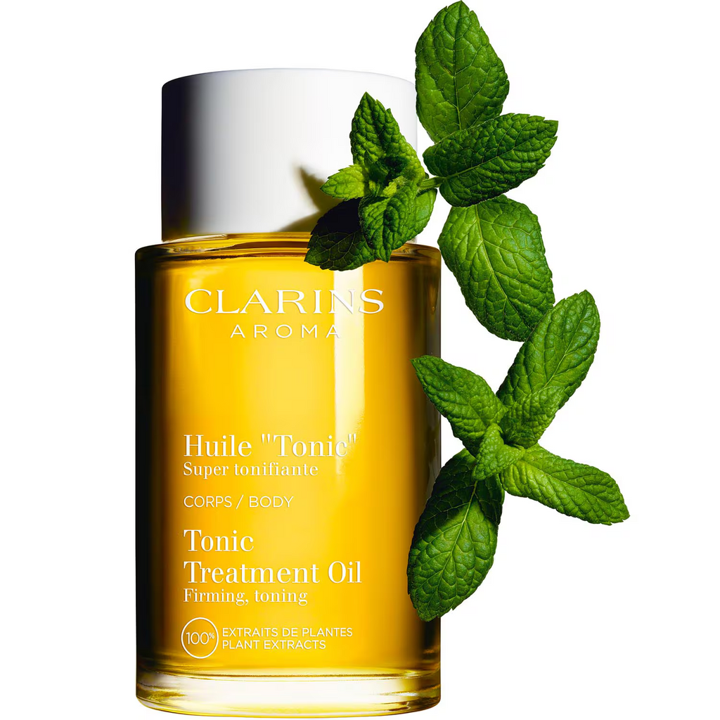Flacon Clarins Huile Tonic Corps 100 ml accompagné de branches de menthe sur fond blanc.