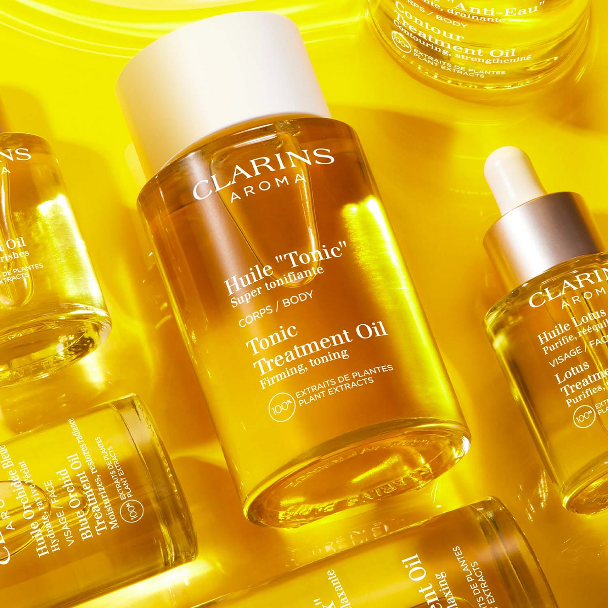 Huile Tonic Corps Clarins parmi plusieurs huiles de la gamme Aroma sur fond jaune.