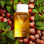 Huile Tonic Corps Clarins 100 ml entourée de noisettes et de feuilles de menthe.