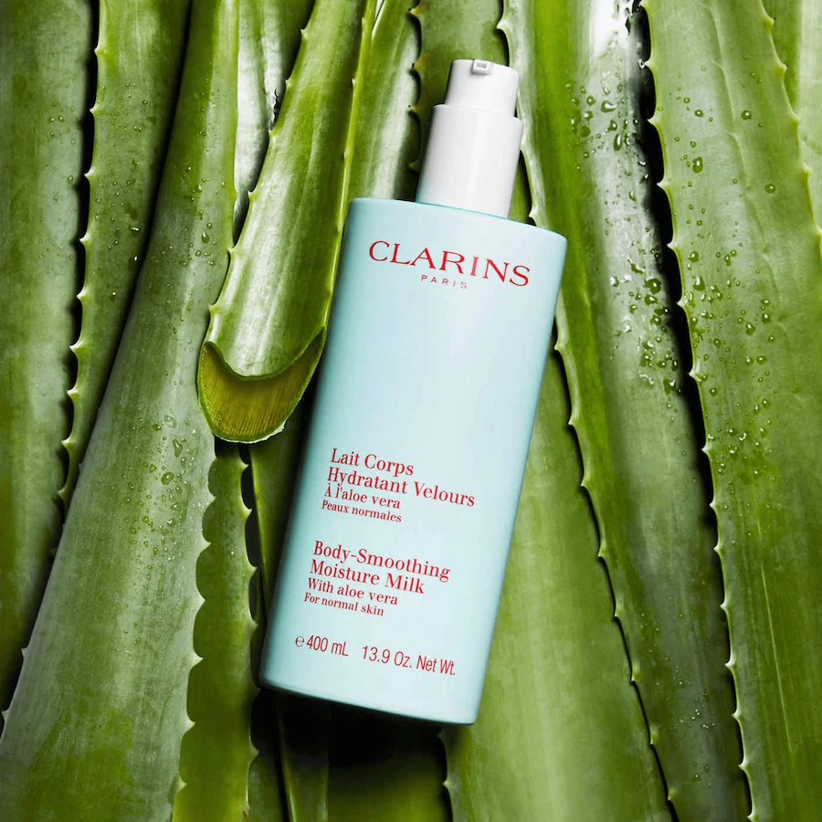 Flacon Clarins Lait Corps Hydratant Velours 400 ml posé sur des feuilles d’aloe vera.