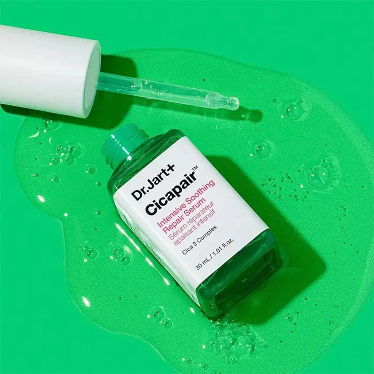Flacon Dr.Jart+ Cicapair Sérum Réparateur Apaisant Intensif 30 ml posé sur une texture de sérum vert translucide, avec pipette.