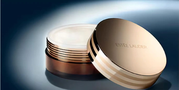Pot ouvert Estée Lauder Advanced Night Cleansing Balm 70 ml, présentant le baume clair et son couvercle doré posé à côté sur fond bleu foncé.